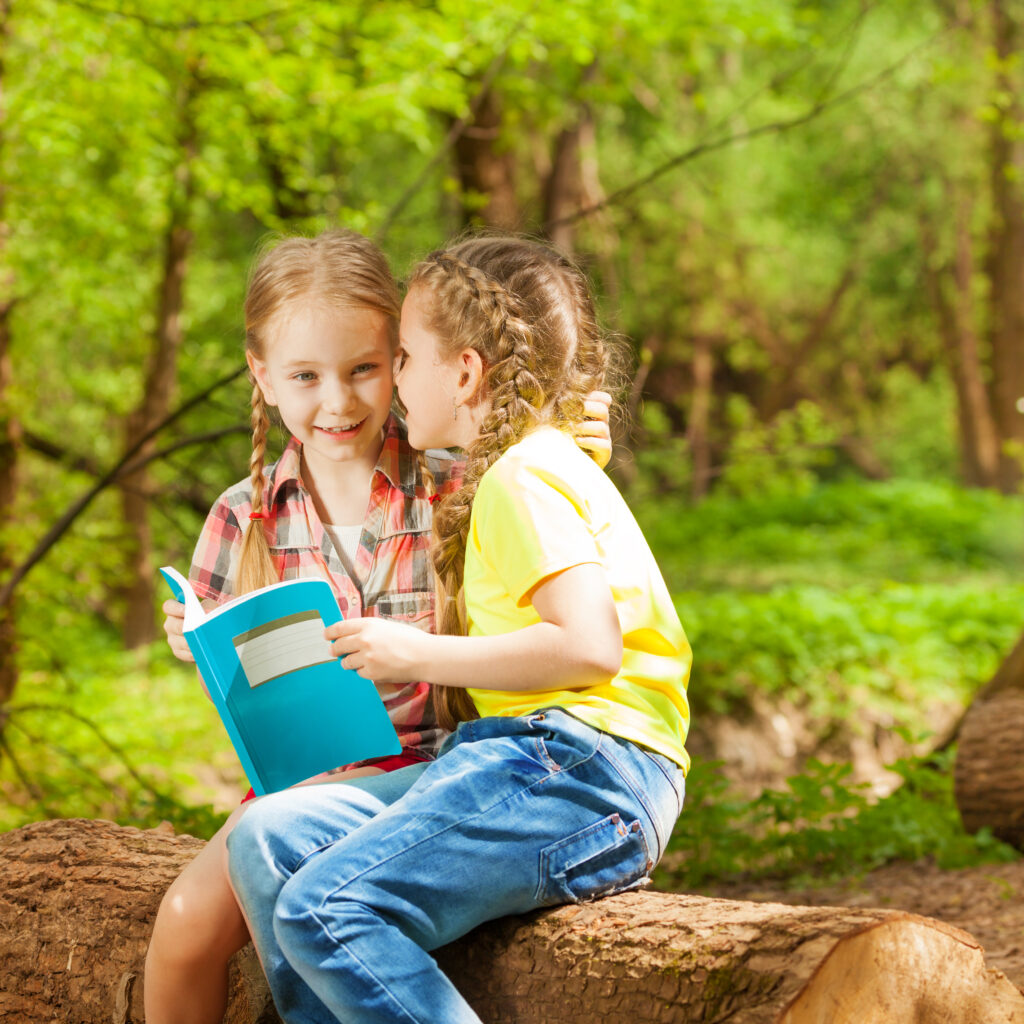 two friends whispering secrets sitting at park